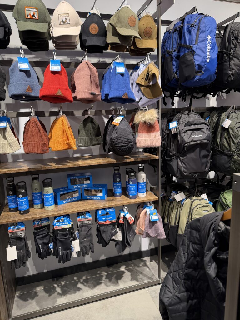 Стенен рафт в магазин Columbia, подреден с зимни шапки, ръкавици, термоси и туристически раници