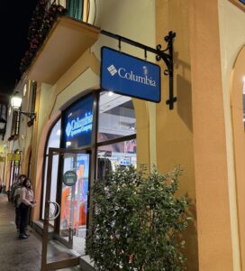 Вечерна снимка на витрина на магазин Columbia Sportswear Company с манекени в зимни туристически дрехи и ярко осветена табел