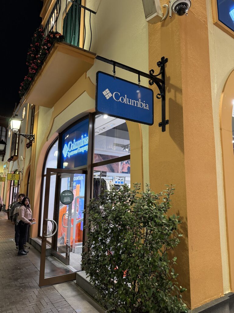 Вечерна снимка на витрина на магазин Columbia Sportswear Company с манекени в зимни туристически дрехи и ярко осветена табел