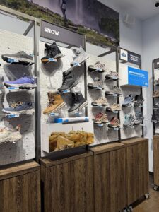 Щанд в магазин Columbia с подредени по стена зимни и туристически обувки и маратонки, секция Snow