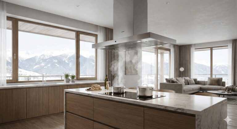 A large stainless steel island range hood mounted above a kitchen island draws steam from pots on an induction hob. Background: a modern living room and large windows with views of snow-capped mountains.