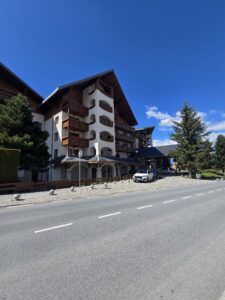 Страничен изглед в перспектива на фасадата на Кемпински Хотел Гранд Арена в Банско с паркирани автомобили.