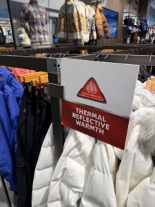 Вечерна снимка на витрина на магазин Columbia Sportswear Company с манекени в зимни туристически дрехи и ярко осветена табел