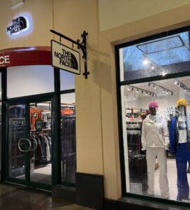 Осветен вход и витрина на магазин The North Face с манекени, облечени в зимни ски якета, панталони и цветни шапки.
