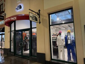 Illuminated entrance and window display of The North Face store with mannequins dressed in winter ski jackets, pants and colorful hats.
