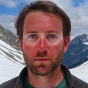 Portrait of a man with a slight blush on his face, standing indoors, without sunglasses.