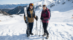 A man wearing Salomon ski gear and a woman wearing winter hiking gear pose on a snowy peak in Pirin above the Bansko ski resort.