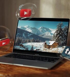 Лаптоп върху дървена маса, показващ видео със зимен пейзаж и хижа в планината, заобиколен от летящи икони на YouTube и TikTok.