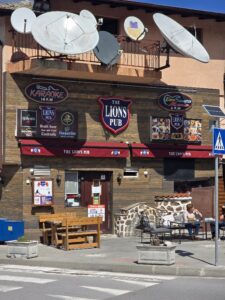 Близък изглед на дървената фасада на The Lions Pub в Банско с табели за караоке, музика на живо и външни маси.