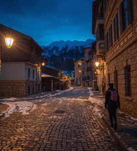 Осветена зимна улица в стария град на Банско през нощта с гледка към Пирин