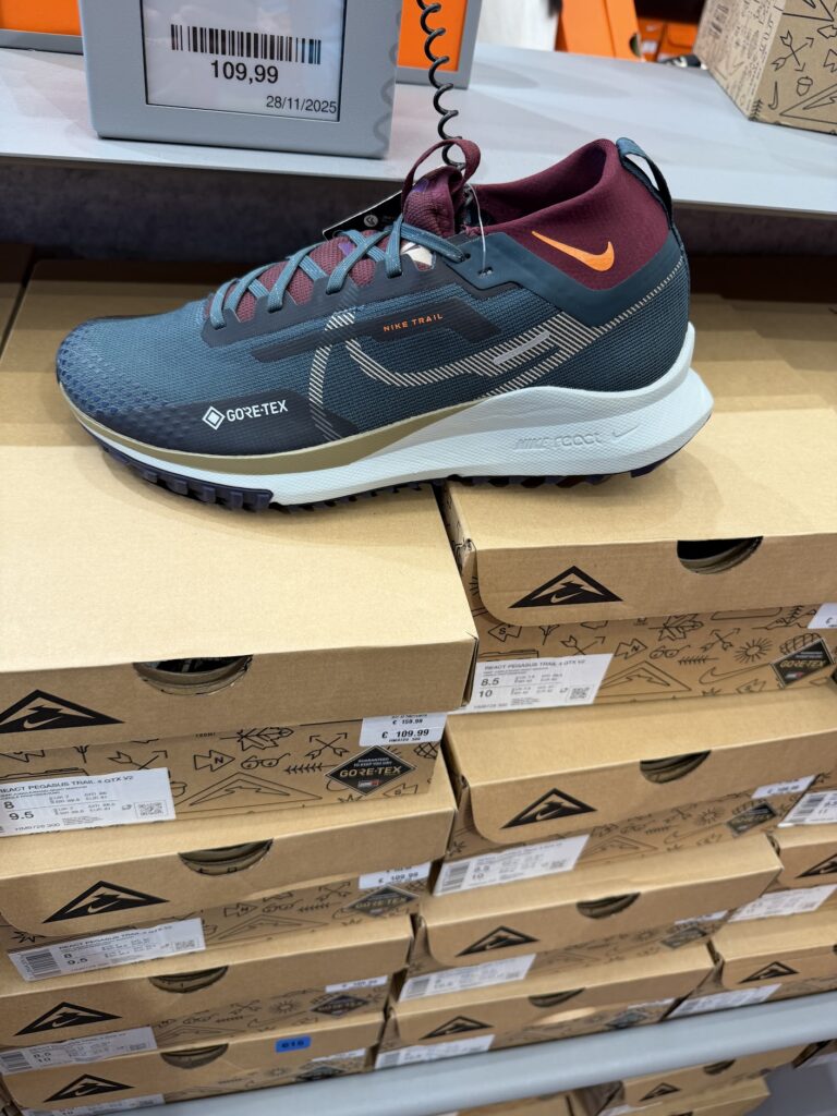 Маратонка Nike Trail с Gore‑Tex в тъмносиньо и бордо, изложена върху кашони с логото на Nike, с видима цена 109,99 евро.