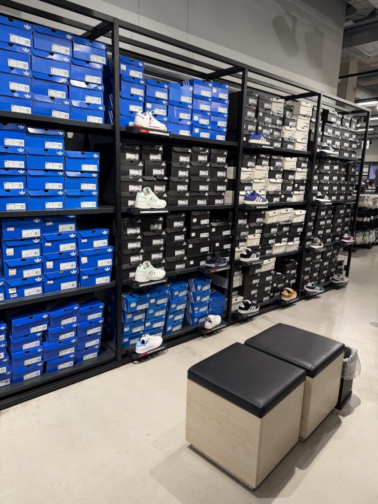 Рафтове с кутии и маратонки Adidas в магазин, с две пуфчета за пробване отпред.