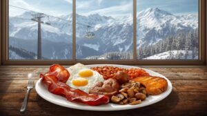 A plate of full English breakfast - fried eggs, bacon, sausages, beans and mushrooms, served on a rustic wooden table in front of a large window with a view of the snow-capped mountain peaks and the gondola lift in Bansko.