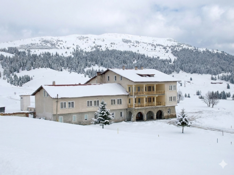 Hristo Smirnenski Hut in winter, covered in snow, with a coniferous forest and Belmeken Peak in the background.