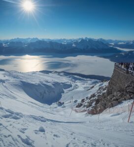Скиори се спускат по стръмната писта Стената на Безбог пред погледа на хората от хижата.