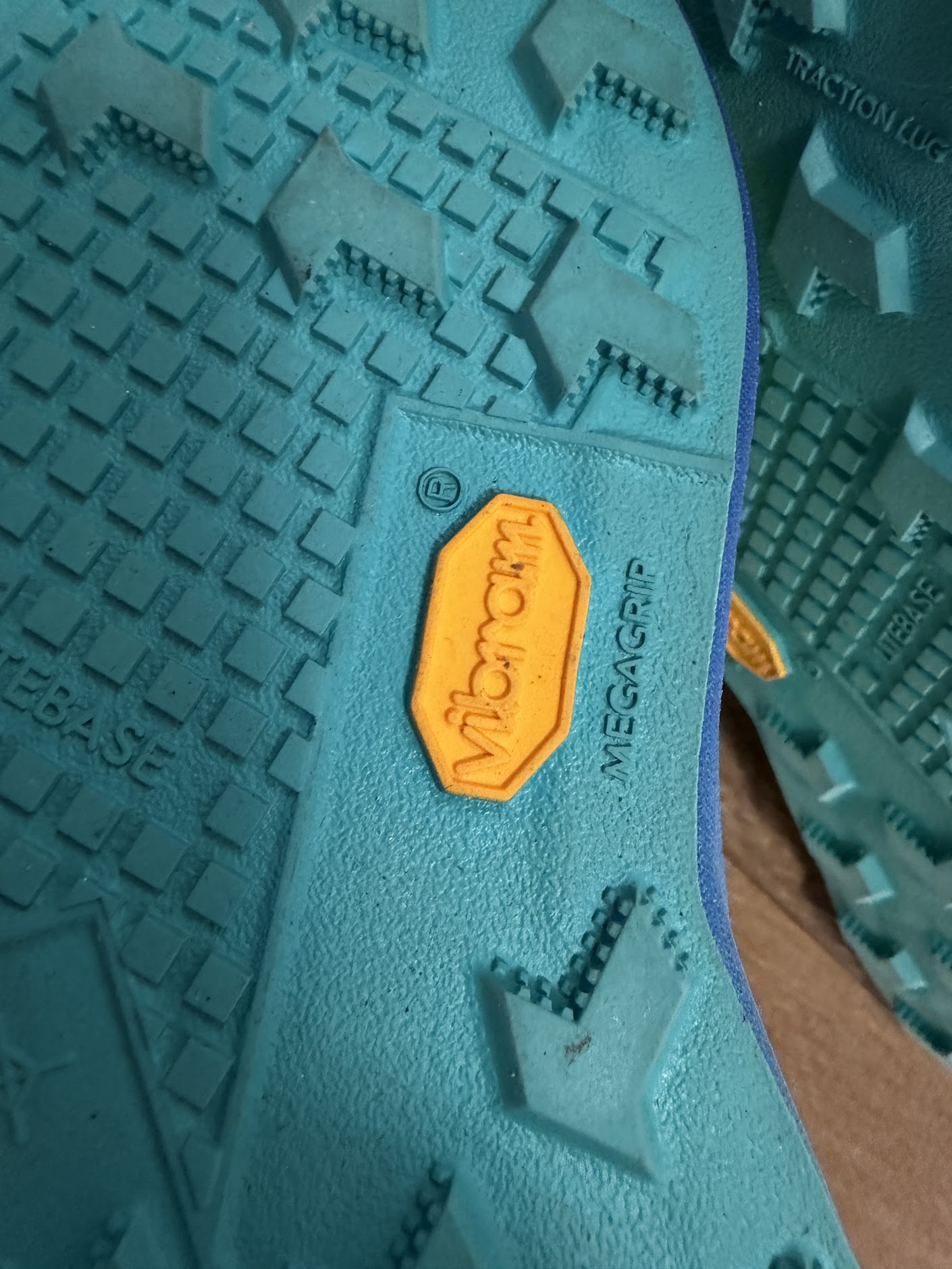 Синя подметка на маратонки Nike Ultrafly с жълто лого Vibram, надписи MegaGrip и Litebase, и карбонова технология Flyplate върху дървен под.