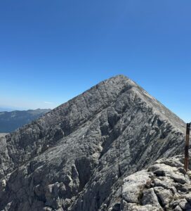 Туристи преминават през тесния карстов ръб Кончето в Пирин, държейки се за металното въже, на фона на връх Бански суходол.