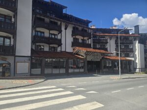 Близък кадър на главния вход на Sport Hotel в Банско с пешеходна пътека отпред.
