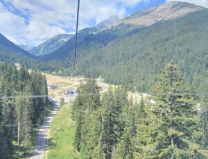 Summer view from a cable car towards a mountain road and Banderishka Polyana resort area in Pirin Mountain, surrounded by green forests.
