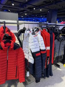 Luxury Toni Sailer ski jackets on a hanger in a store – red and white model with the black chamois logo.