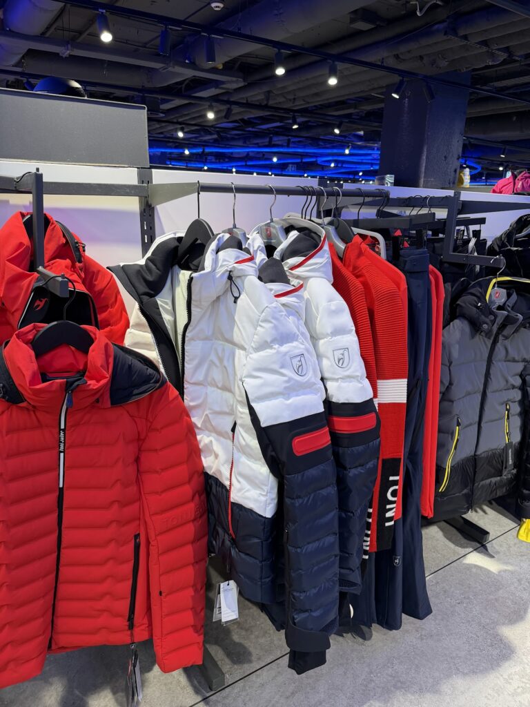 Luxury Toni Sailer ski jackets on a hanger in a store – red and white model with the black chamois logo.