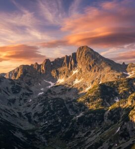 Внушителният гранитен връх Джангал в Пирин планина, осветен от слънце, с драматични облаци в синьото небе.