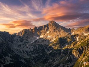 The imposing granite peak of Jangal in the Pirin Mountains, illuminated by the sun, with dramatic clouds in the blue sky.