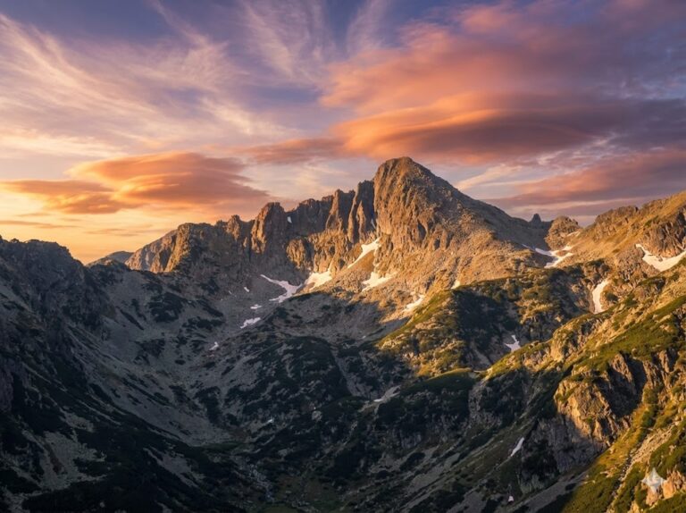 The imposing granite peak of Jangal in the Pirin Mountains, illuminated by the sun, with dramatic clouds in the blue sky.
