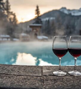 Чаши с червено вино до външен минерален басейн в Банско на фона на заснежен Пирин.