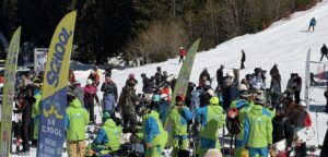 Ски инструктори в зелени екипи организират групи от скиори край знамена на ски училища на пистата в Банско.