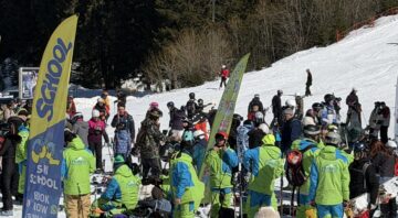 Ski instructors in green outfits organize groups of skiers near ski school flags on the slope in Bansko.