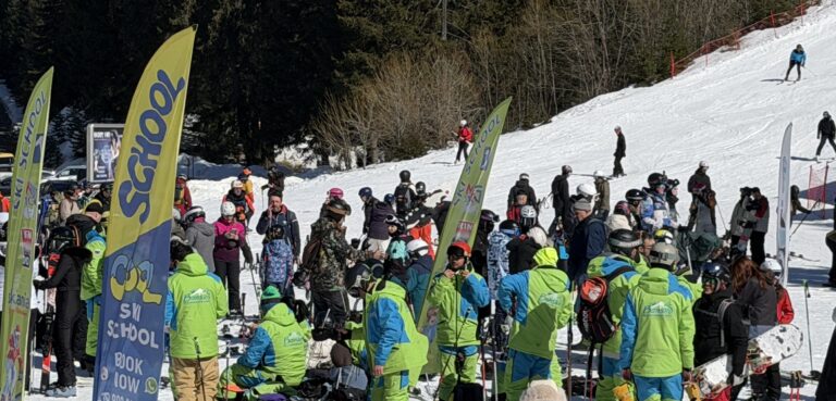 Ски инструктори в зелени екипи организират групи от скиори край знамена на ски училища на пистата в Банско.