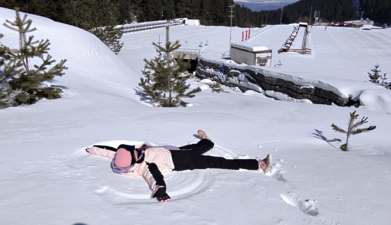 Човек прави снежен ангел на сняг в Банско с планина в Пирин на заден план