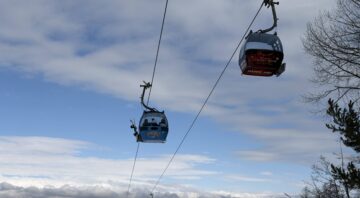 Cable car in Bansko with branded gondolas moving on steel cables against a blue sky with white clouds and a view of the mountain and the rooftops of the city