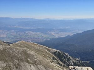 Panoramic view from high on the rocky peak of Pirin Mountain towards the Razlog Valley, the town of Bansko and the distant mountain ranges of Rila and Rhodope Mountains in a blue haze.