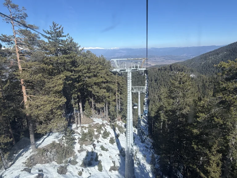 Изглед от кабинката на лифта в Банско към стоманените стълбове и въжето над заснежената гора.