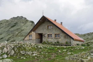 The massive stone building of the Tevno Lake shelter with a steep metal roof, located amidst the harsh rocky landscape and moraines high in the Pirin Mountains.