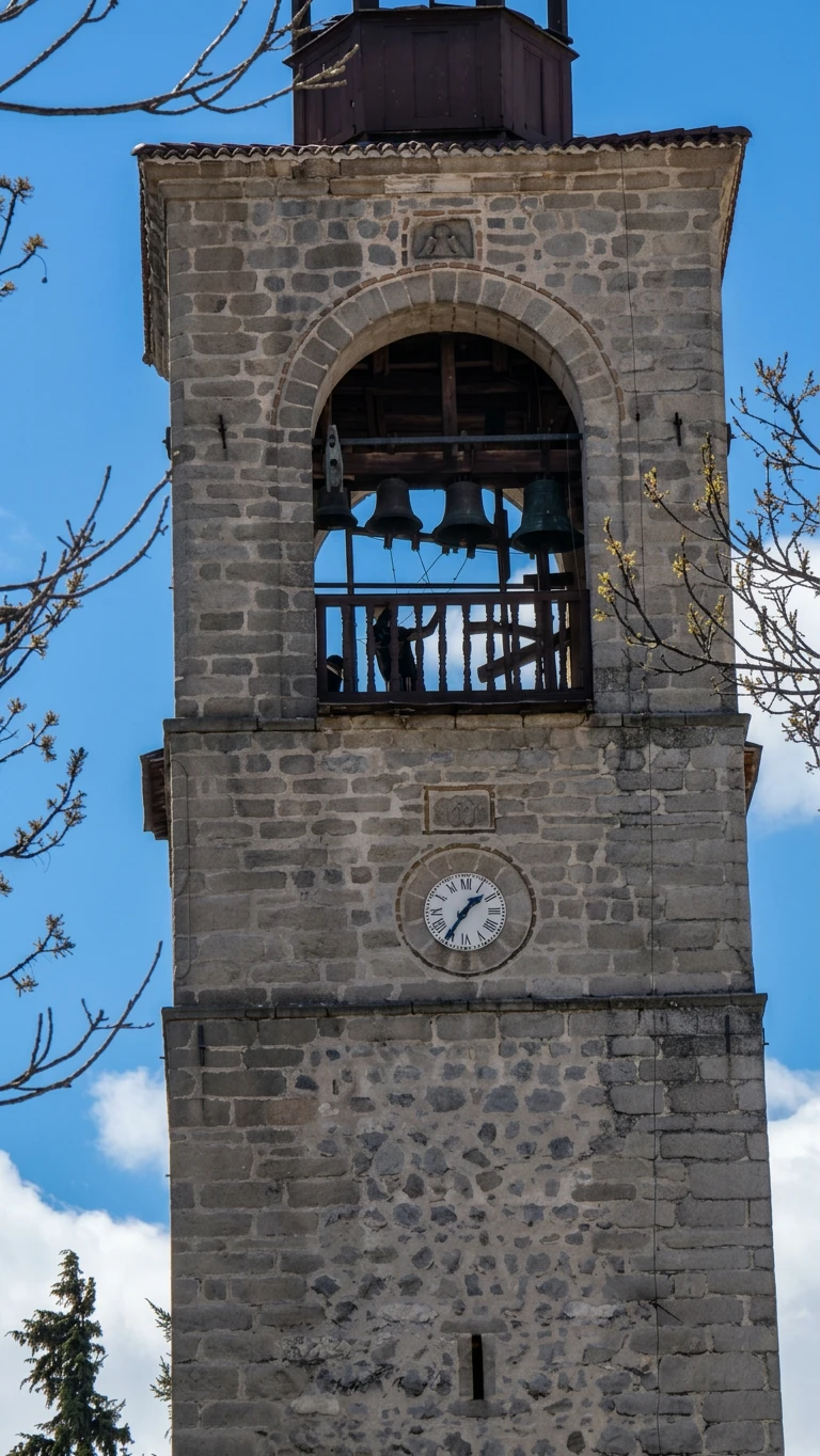 The bell tower of the Holy Trinity Church in Bansko - a stone tower with bells and a clock with Roman numerals, 1850.