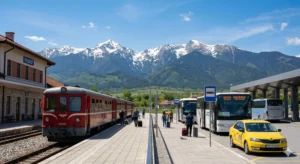 An image of the joint railway and bus station in the town of Razlog, showing the narrow gauge railway, buses to Bansko, and taxis, beneath the majestic, snow-capped peaks of the Pirin Mountains on a sunny day.