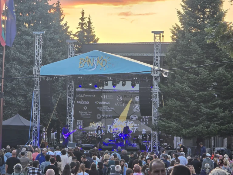 Концерт под открытым небом на фестивале Bansko Rock Fest в Банско, Болгария, с участием исполнителей на сцене перед большой толпой зрителей на закате.
