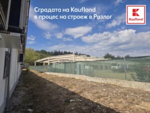 Строителна площадка, показваща бетонната конструкция (скелет) на сграда в строеж, заградена със зелена предпазна мрежа, на фона на гора.